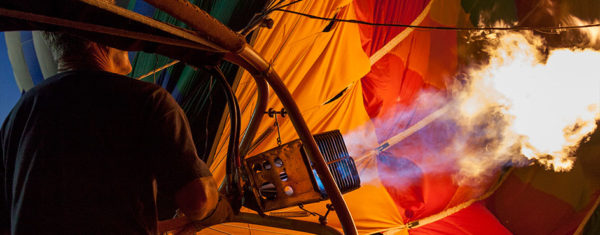 Hot air balloon being filled with flames to create heat. Man on the left operating the hot air dispenser. Image is in full colour.